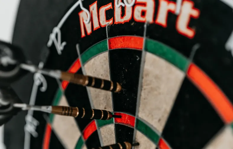 A close up image of a dartboard with three darts in it. One in the 20 point area, one in the triple 20, and the last one in the 1 point area